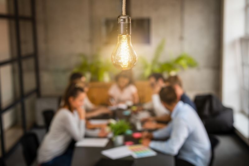 Bright Light bulb hanging from a ceiling above a table of young innovators